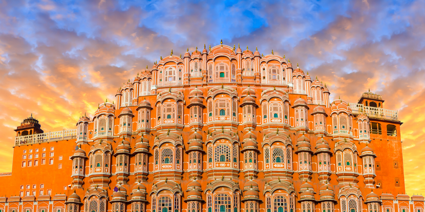 Hawa Mahal, the Palace of Winds, in Jaipur, India, with its honeycomb pink-and-orange sandstone facade glowing beneath a dramatic sunset sky